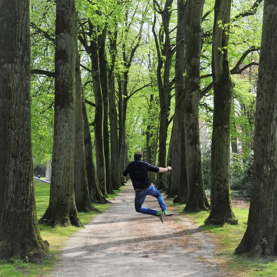 Maarten springt in de lucht op een bospad tussen hoge bomen